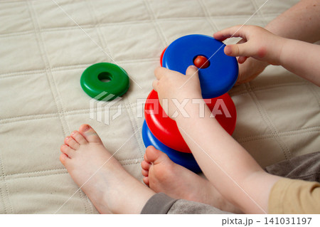Two year old focusing on ring stacking playing with plastic pyramid toy. Logic and thinking skills growth. Bright colors attract attention. Fine motor practice 141031197