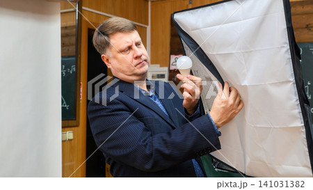 Photographer inspecting a burnt-out studio light bulb in a professional photo studio lighting fixture Photographer inspecting a burnt-out studio light bulb in a professional photo studio lighting fixture 141031382