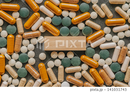 Top view pattern of colorful pharmaceutical pills and dietary supplement capsules arranged around a blank rectangular wooden block for copy space text Top view pattern of colorful pharmaceutical pills and dietary supplement capsules arranged around a blank rectangular wooden block for copy space text 141031743