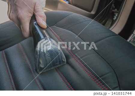 Horizontal close up shot of a man cleaning a black fabric car seat upholstery with red stitching details using a professional vacuum water extraction machine nozzle Horizontal close up shot of a man cleaning a black fabric car seat upholstery with red stitching details using a professional vacuum water extraction machine nozzle 141031744