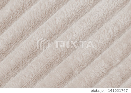 Horizontal close up flat lay shot of a cozy beige plush fleece blanket fabric texture with distinct diagonal ribbed rows of soft fluffy synthetic fur material Horizontal close up flat lay shot of a cozy beige plush fleece blanket fabric texture with distinct diagonal ribbed rows of soft fluffy synthetic fur material 141031747