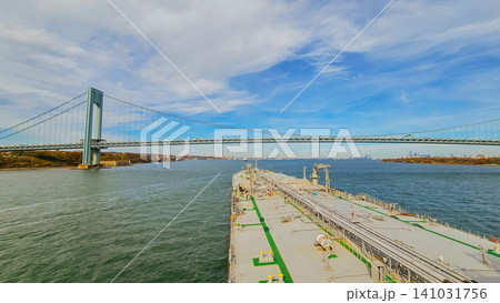 Horizontal high angle shot of a large commercial cargo tanker deck sailing under the massive verrazzano narrows suspension bridge in new york harbor on a sunny day Horizontal high angle shot of a large commercial cargo tanker deck sailing under the massive verrazzano narrows suspension bridge in new york harbor on a sunny day 141031756