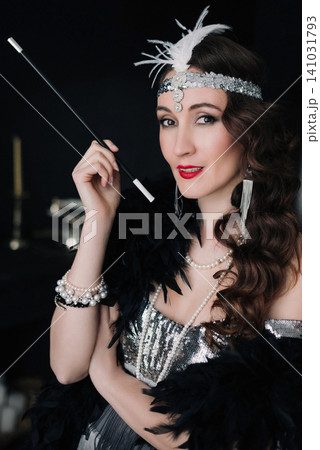 Elegant girl in 1920s flapper outfit holding a long cigarette holder Elegant girl in 1920s flapper outfit holding a long cigarette holder 141031793