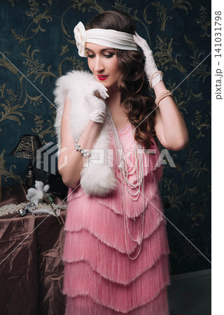Elegant young woman in pink flapper dress with white fur and pearls Elegant young woman in pink flapper dress with white fur and pearls 141031798