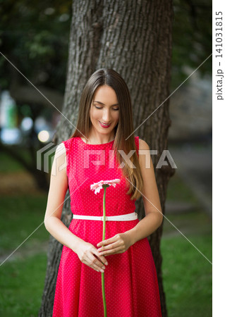 Woman in red polka dot dress looking at a pink daisy 141031815