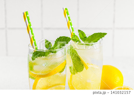 Homemade lemonade with fresh lemon slices, mint and ice in glasses on white tile kitchen background 141032157