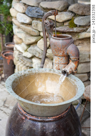Rusty Vintage Manual Water Pump in Front of Stone Wall 141032398