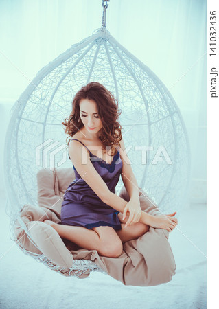 Young girl in blue nightshirt sitting in white hanging cocoon chair Young girl in blue nightshirt sitting in white hanging cocoon chair 141032436