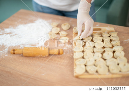 Woman in gloves arranging handmade dumplings on a wooden board 141032535