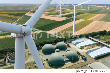 Green energy synergy. Close-up of wind turbine with biogas plant infrastructure in the background Green energy synergy. Close-up of wind turbine with biogas plant infrastructure in the background 141032773