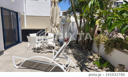 Modern holiday apartment patio with sun loungers, outdoor dining area and tropical garden in Protaras, Cyprus. Bright Mediterranean vacation accommodation on a sunny day. 141032780
