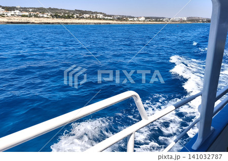 A side view of a boat leaving a foaming wake on the endless blue sea, a sea voyage, adventure and sunny summer sailing on the open sea. A side view of a boat leaving a foaming wake on the endless blue sea, a sea voyage, adventure and sunny summer sailing on the open sea. 141032787