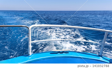 Boat stern with foamy wake on the deep blue sea during a sunny summer day. View from the deck of a moving vessel on open water, symbolizing travel, tourism, and marine adventure. Boat stern with foamy wake on the deep blue sea during a sunny summer day. View from the deck of a moving vessel on open water, symbolizing travel, tourism, and marine adventure. 141032788