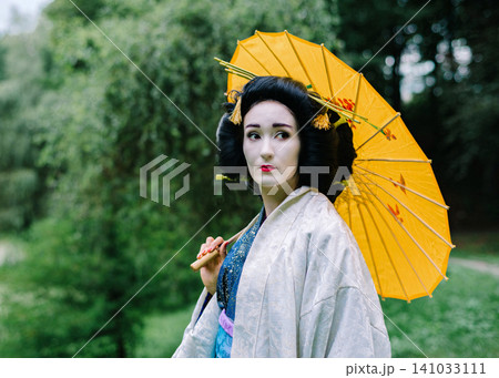 Artistic portrait of a woman in geisha kimono with yellow umbrella under willow tree Artistic portrait of a woman in geisha kimono with yellow umbrella under willow tree 141033111
