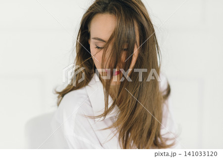 a beautiful sexy girl in a white men's shirt poses near a wall background 141033120