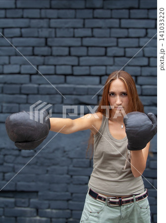 Young woman in boxing gloves throwing a punch against dark brick wall Young woman in boxing gloves throwing a punch against dark brick wall 141033220
