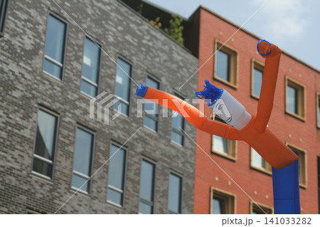 Orange and blue inflatable tube men in front of modern brick buildings Orange and blue inflatable tube men in front of modern brick buildings 141033282