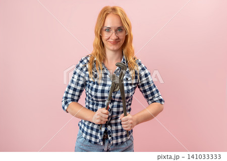 Young woman wearing a plaid shirt and safety glasses, confidently holding a large pipe wrench, embodying strength and capability for home improvement and skilled work Young woman wearing a plaid shirt and safety glasses, confidently holding a large pipe wrench, embodying strength and capability for home improvement and skilled work 141033333