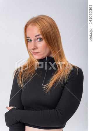 Young woman posing in studio against a clear background, crossing her arms and making a face conveying curiosity, mild skepticism, or thoughtful consideration Young woman posing in studio against a clear background, crossing her arms and making a face conveying curiosity, mild skepticism, or thoughtful consideration 141033365