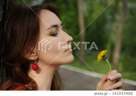 Beautiful woman with ladybug earrings smelling a yellow dandelion Beautiful woman with ladybug earrings smelling a yellow dandelion 141033488