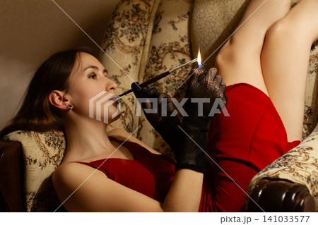 Vintage-style portrait of a woman lighting a cigarette in a red dress Vintage-style portrait of a woman lighting a cigarette in a red dress 141033577