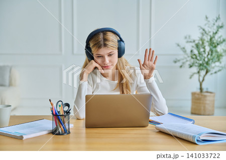Teenage girl in headphones waving hand to laptop 141033722