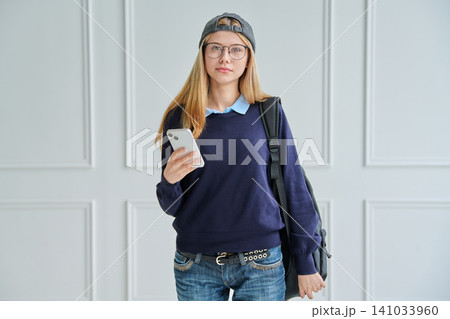 Smiling teenage student with backpack holding phone Smiling teenage student with backpack holding phone 141033960