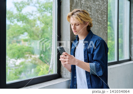 Serious teenage boy using a smartphone by window 141034064