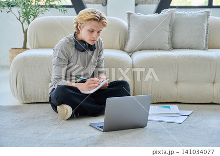 Young student studying with laptop on floor at home Young student studying with laptop on floor at home 141034077