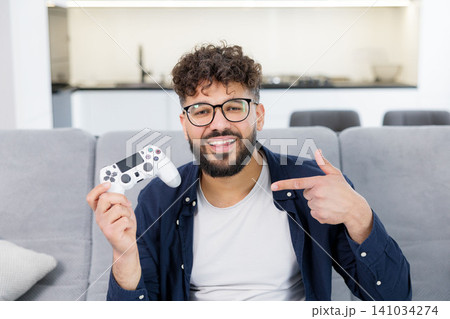 Happy man holding gaming controller pointing at it 141034274