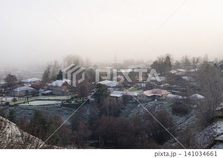 The image depicts dwellings with tiled roofs, enveloped in a dense mist The image depicts dwellings with tiled roofs, enveloped in a dense mist 141034661