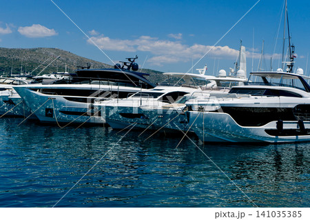 Luxury motor yachts lined up in a modern marina with calm blue water, clear skies and coastal hills, showcasing premium leisure and marine lifestyle 141035385