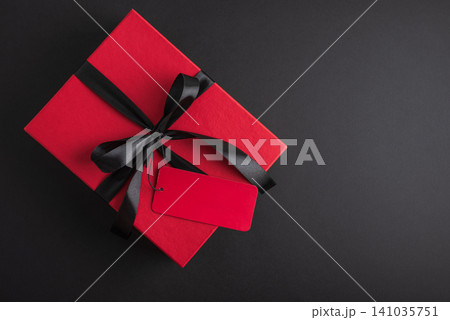 Red gift box with black ribbon and blank tag on dark background Red gift box with black ribbon and blank tag on dark background 141035751