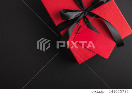 Red gift box with black ribbon and blank tag on dark background Red gift box with black ribbon and blank tag on dark background 141035753