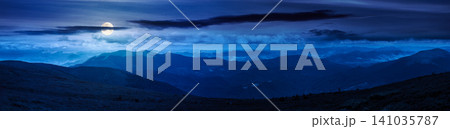 beautiful panorama of mountainous landscape at night. full moon over wide view of cloudy sky over the grassy slope of a mountain ridge. mysterious summer weather. adventure tourism in highland 141035787