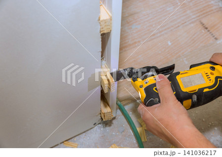 Worker uses power saw to cut wood to fit into construction project in busy work area. Worker uses power saw to cut wood to fit into construction project in busy work area. 141036217
