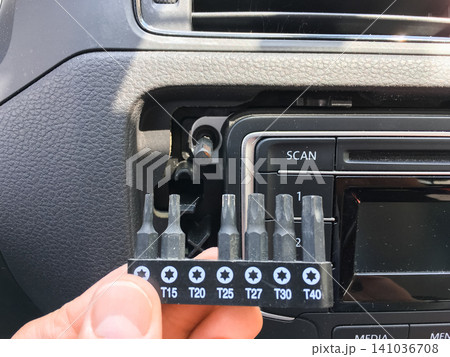 Hand holding a set of Torx screwdriver bits in front of a car radio in the dashboard. Hand holding a set of Torx screwdriver bits in front of a car radio in the dashboard. 141036708
