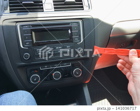 Hand prying off the trim around a car radio using a red plastic tool in the dashboard. 141036717
