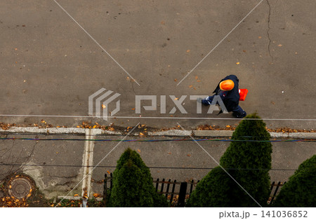 Top view of electrician or power grid worker walking on city street. Utility technician in hard hat carrying toolbox, electricity maintenance and energy infrastructure rehabilitation concept Top view of electrician or power grid worker walking on city street. Utility technician in hard hat carrying toolbox, electricity maintenance and energy infrastructure rehabilitation concept 141036852