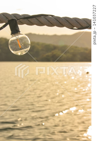 夕暮れの水辺に吊るされたおしゃれな電球、リゾート、夕日、背景素材、縦位置 夕暮れの水辺に吊るされたおしゃれな電球、リゾート、夕日、背景素材、縦位置 141037227