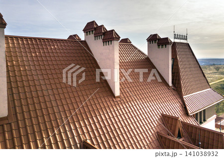 Close-up detail of building steep shingle roof and brick plastered chimneys on house top with metal tile roof. Roofing, repair and renovation work. Close-up detail of building steep shingle roof and brick plastered chimneys on house top with metal tile roof. Roofing, repair and renovation work. 141038932