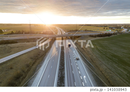 Aerial view of modern highway road intersection at dawn on rural landscape and raising sun background. Drone photography. Aerial view of modern highway road intersection at dawn on rural landscape and raising sun background. Drone photography. 141038943