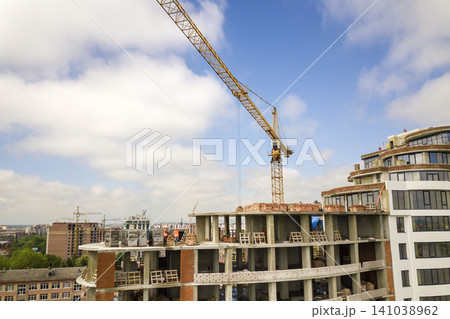 Apartment or office tall building under construction. Brick walls, glass windows, scaffolding and concrete support pillars. Tower crane on bright blue sky copy space background. 141038962