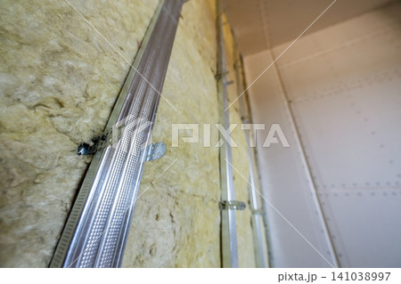 Wall of a room under renovation with mineral rock wool insulation and metal frame prepared for drywall plates. Wall of a room under renovation with mineral rock wool insulation and metal frame prepared for drywall plates. 141038997