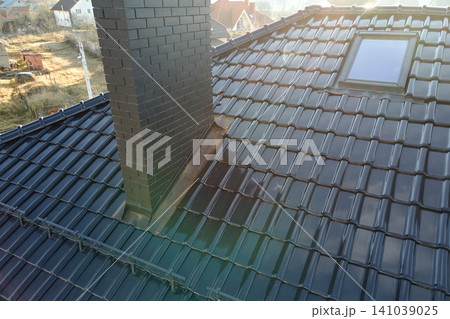 Closeup of attic window and brick chimney on house roof top covered with ceramic shingles. Tiled covering of building 141039025