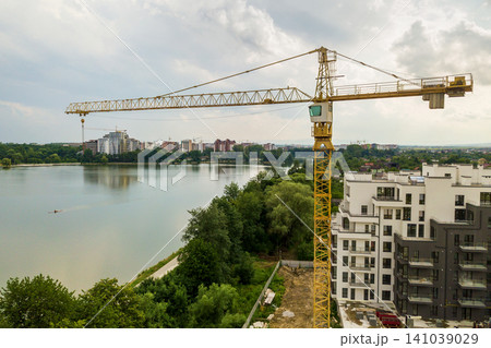 Aerial view of tower lifting crane and concrete frame of tall apartment residential building under construction in a city. Urban development and real estate growth concept. 141039029