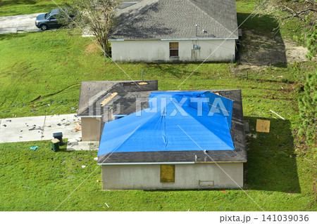 Hurricane Ian damaged house rooftop covered with protective plastic tarp against rain water leaking until replacement of asphalt shingles. Aftermath of natural disaster Hurricane Ian damaged house rooftop covered with protective plastic tarp against rain water leaking until replacement of asphalt shingles. Aftermath of natural disaster 141039036