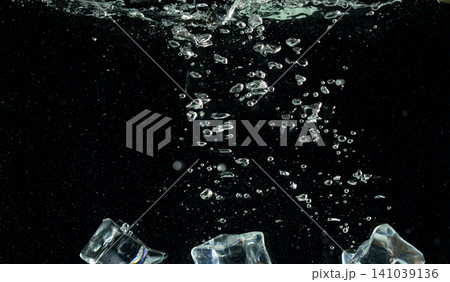 Falling ice cube pieces with water splashing in midair on a transparent, isolated black background. Ice cubes drop into water with air bubbles scatter splashing 141039136