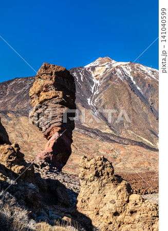 Scenic view of the famous Roque Cinchado rock formation with the snow-capped Mount Teide volcano under a clear blue sky in Tenerife, Spain. Scenic view of the famous Roque Cinchado rock formation with the snow-capped Mount Teide volcano under a clear blue sky in Tenerife, Spain. 141040599