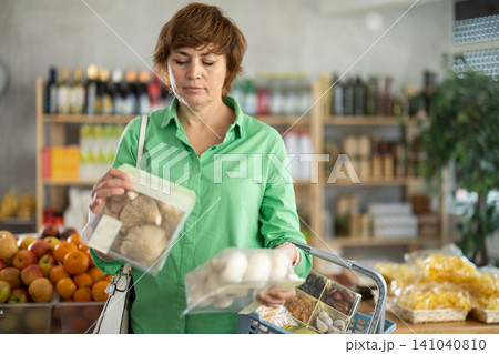 Woman holding plastic containers with oyster mushrooms and champignons, thinking about buying Woman holding plastic containers with oyster mushrooms and champignons, thinking about buying 141040810